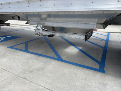 Trailer underside showing bulk grain hopper connection with a measurement gauge and metal frame, isolated in a parking area.