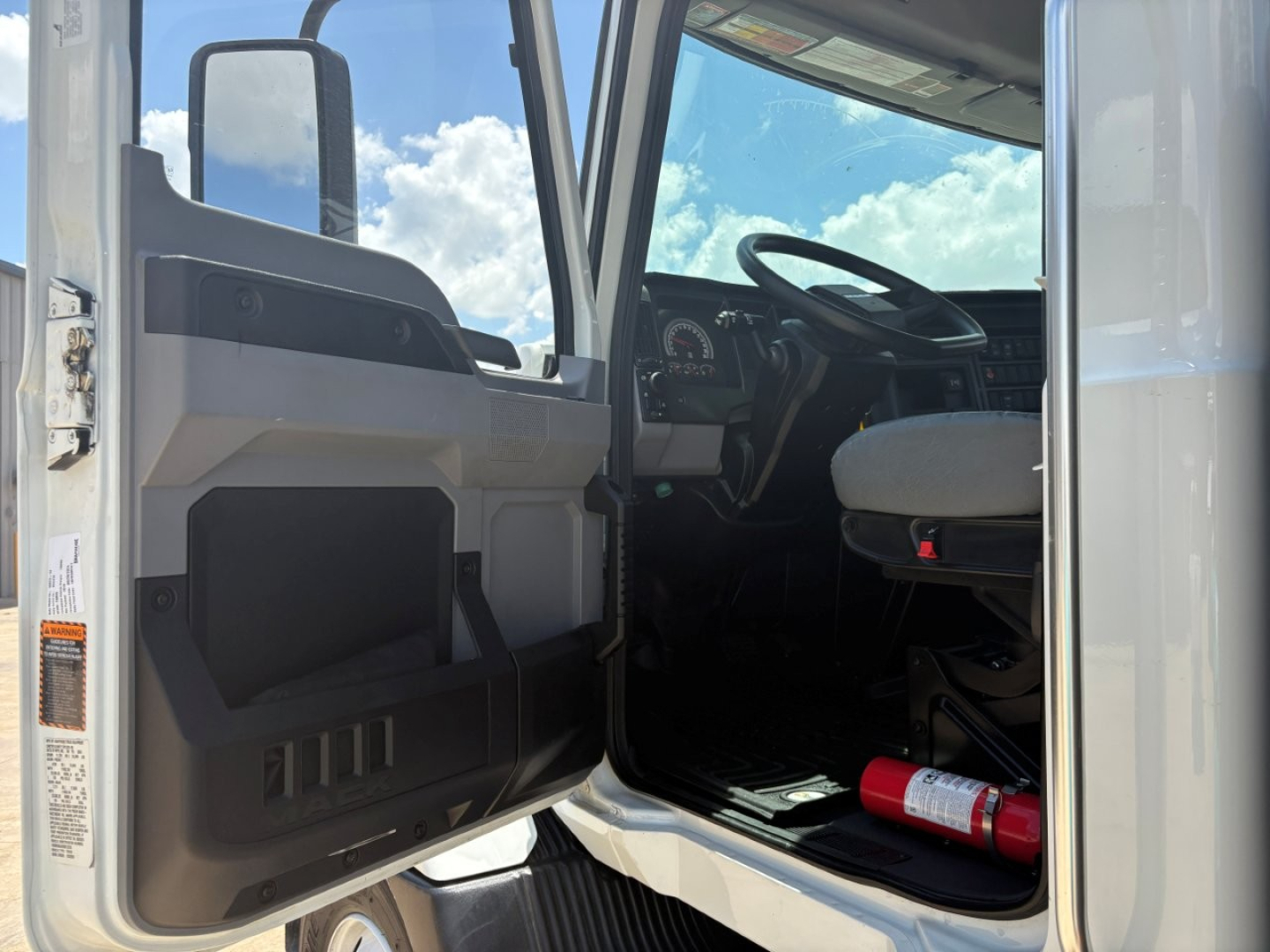Cab interior of a 2024 Mack MD6 truck showing open driver door, steering wheel, and dashboard.