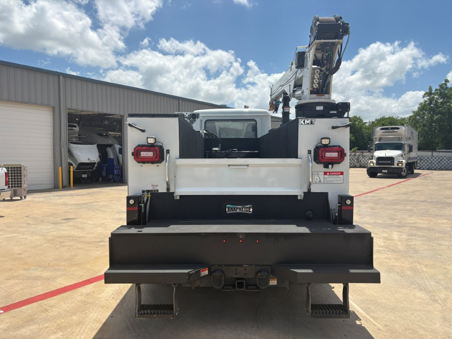 Rear view of a 2024 Mack MD6 service truck with a mounted crane and heavy-duty bumper, in a dealership lot.