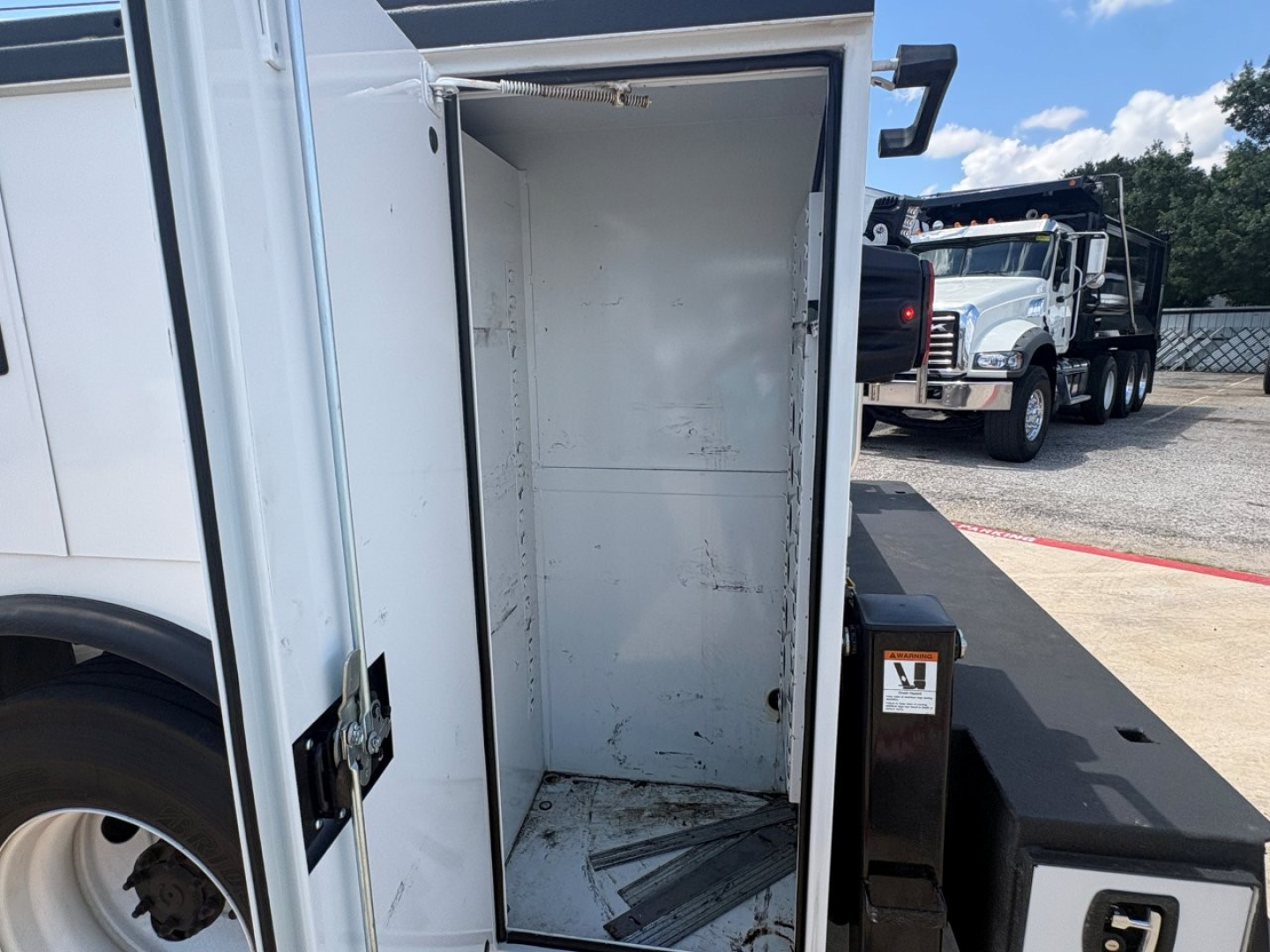 Truck service bed interior showing empty metal cargo area with white walls and a textured floor on a white and black Mack MD6 chassis.