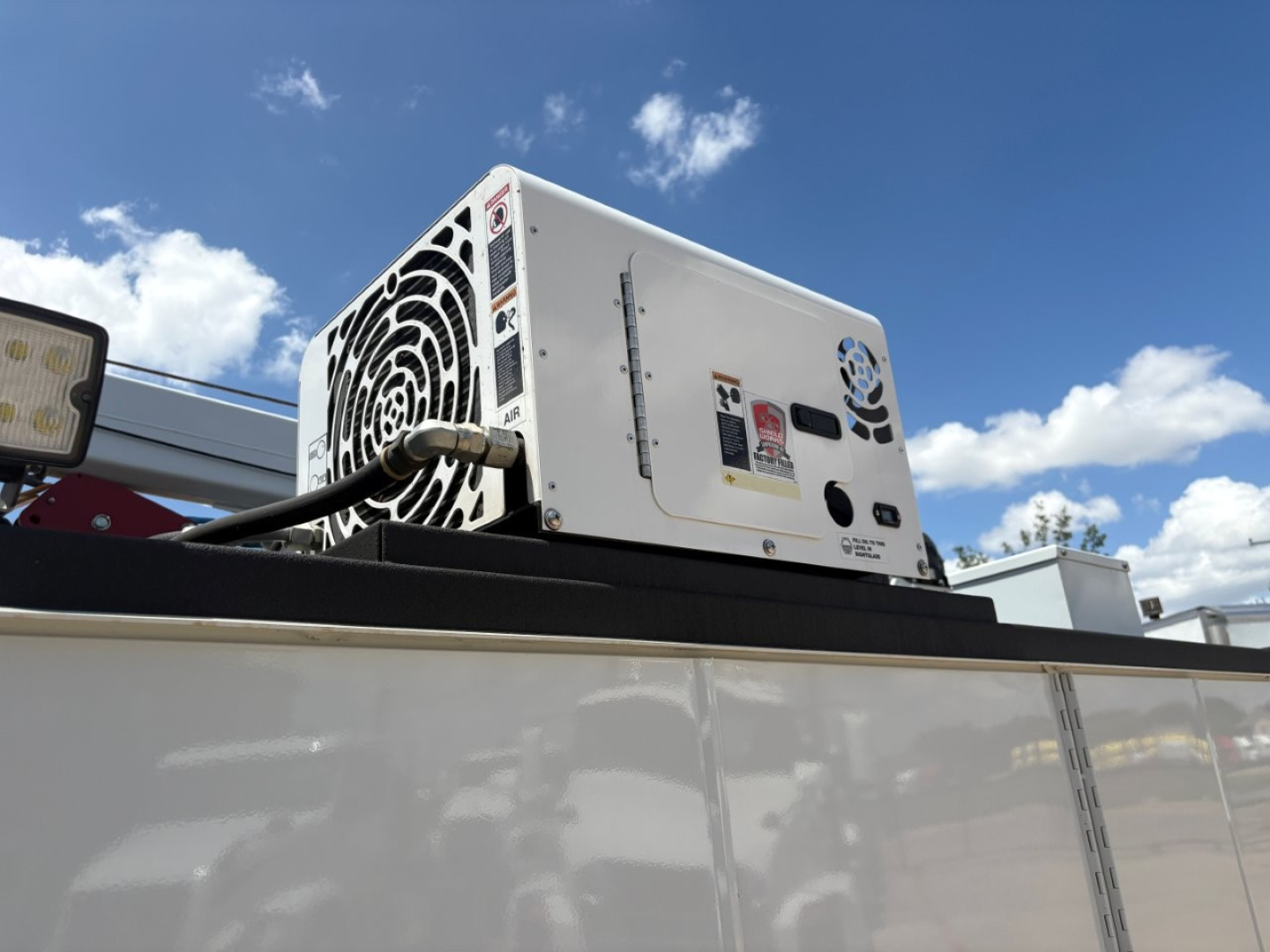 External view of a vehicle cooling unit mounted on a utility truck body. The unit has a circular fan grill, power cable, and control panel with labels.