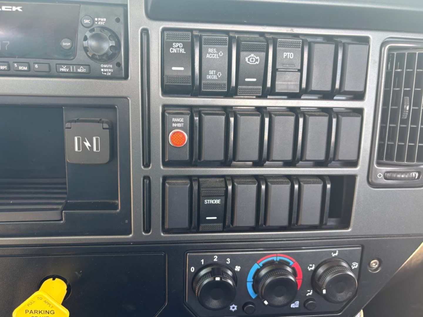 Dashboard control panel of a 2024 Mack MD6 showing switches, knobs, and a circular blue-red climate control dial.