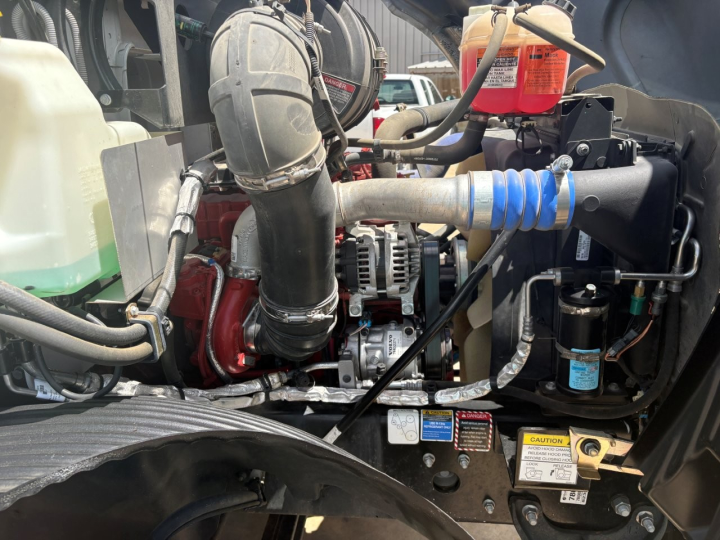 Mack MD6 engine bay view showing intercooler piping, air intake hose, alternator, coolant reservoir, and oil reservoir labels visible.