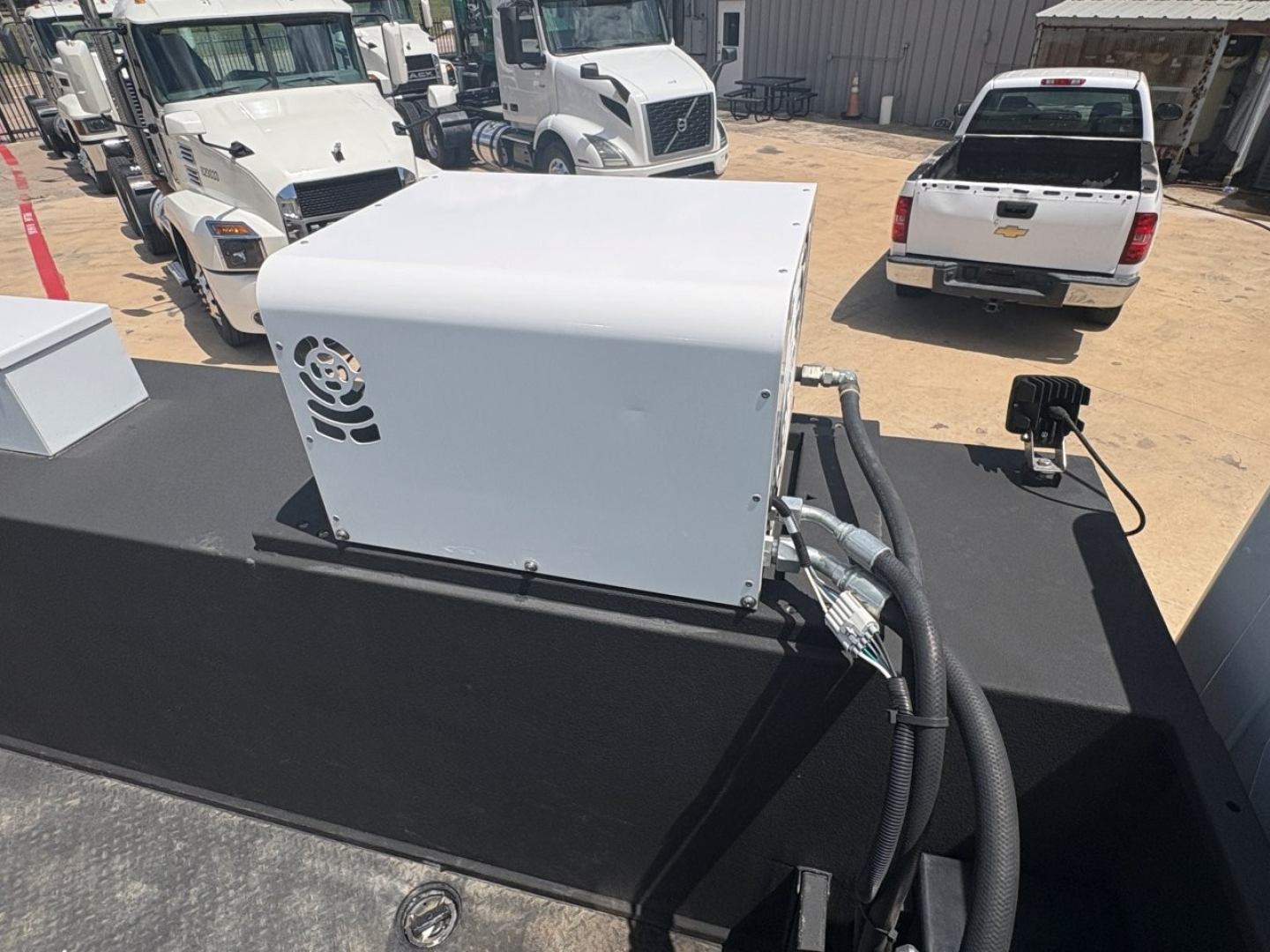 Equipment image showing a white generator or auxiliary unit on a flatbed of a Mack MD6 truck setup. Visible hoses and cables connected to the unit with a fan vent on the side.