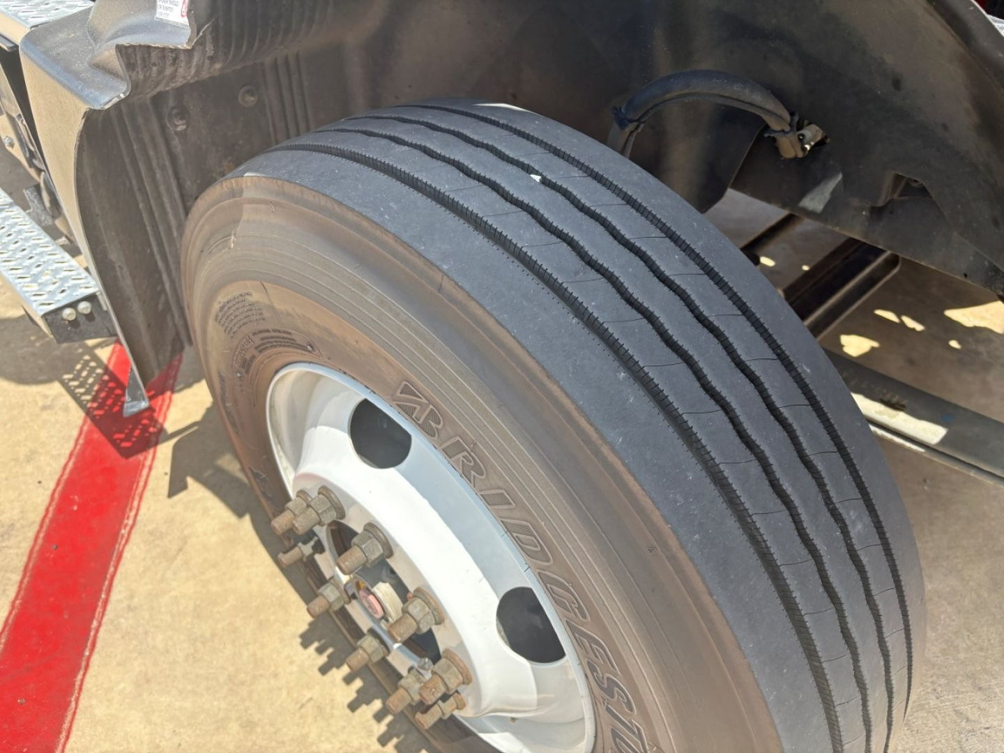 Front left tire of a Mack MD6 truck showing wheel hub and lug nuts with tread pattern and alloy rim.