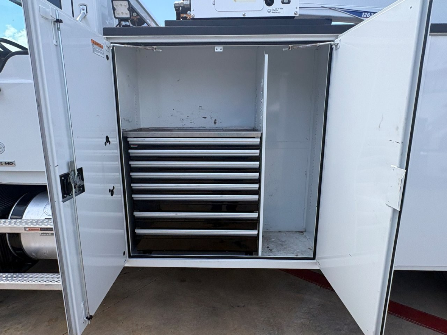 Truck service body showing a cabinet with multiple metal drawers inside, open double doors on a Mack MD6 utility truck.