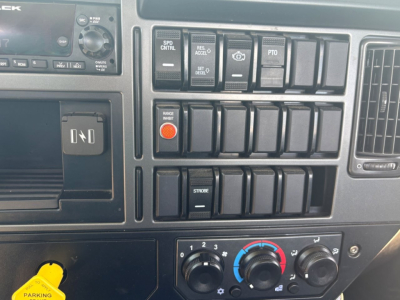 Dashboard control panel of a 2024 Mack MD6 showing switches, knobs, and a circular blue-red climate control dial.