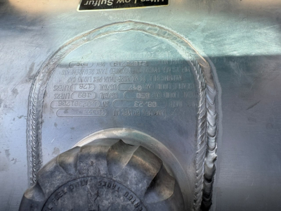 Mack MD6 component area showing welded tank/plate with embossed specification label and large braided hose/connector.