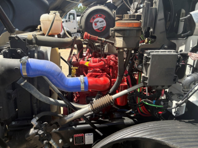 Engine bay of a Mack MD6 showing blue coolant hose, red engine block, various hoses and wiring in-service utility truck.