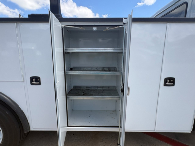 Service/utility truck body with an open side cabinet featuring multiple metal shelves and an empty top shelf.