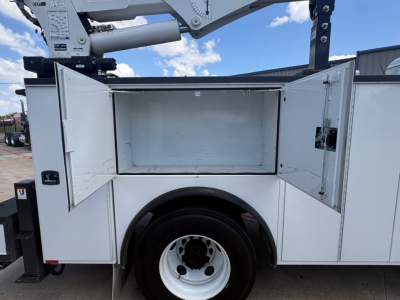 Mack MD6 service body truck side compartments open showing empty storage bay and hydraulic lifting mechanism above.