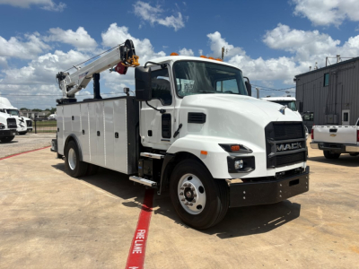 Mack MD6 service truck with crane in white, side utility body, and front grille showing Mack emblem; cab door, large side compartments, and crane mounted over rear bed.
