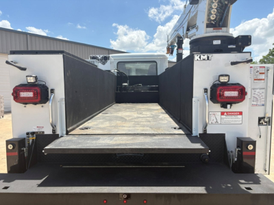 Mack MD6 service/utility truck bed with flatbed and side rails, rear view showing hydraulic crane and platform, taillights visible.