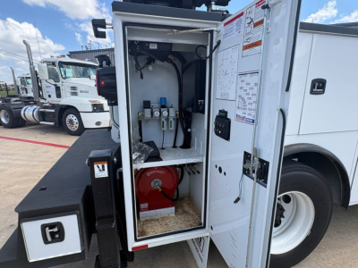 Service/utility truck rear cabinet showing equipment bay with hoses, gauges, and a red reel. Door panel has diagrams and labels.