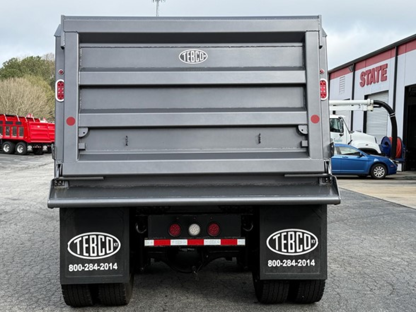 Rear view of a new Western Star 47X dump truck showing TEBCO mud flaps with TEBCO branding and contact number, hydraulic tailgate, and rear lights.