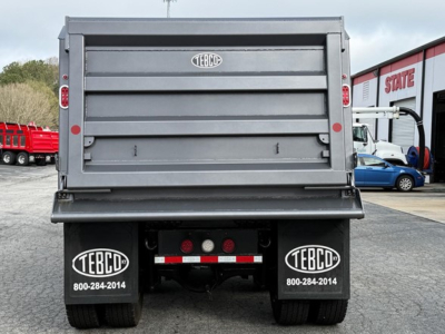 Rear view of a new Western Star 47X dump truck showing TEBCO mud flaps with TEBCO branding and contact number, hydraulic tailgate, and rear lights.