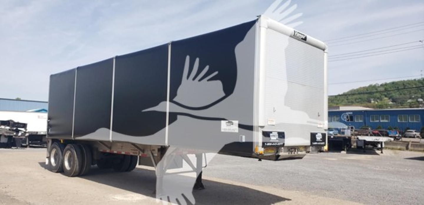 Trailer showing rear and side, curtainside with white graphic birds on dark panels. visible logos and rear bumper.