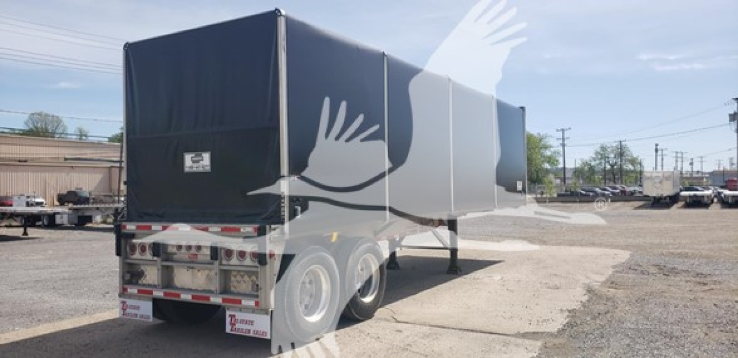 Trailer rear and side view showing curtainside Big Bubba with dual rear axles and white reflective tape, yard in background.