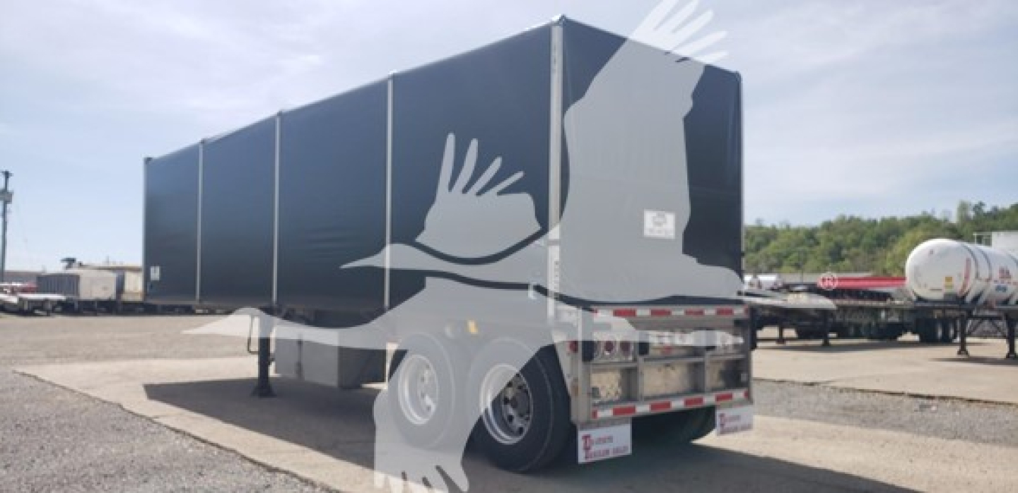 Curtainside trailer showing rear and side edges with VIN and stock number not visible; exterior panels dark blue, dual rear wheels, frame, and suspension visible.