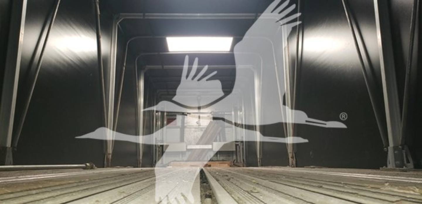 Trailer interior view showing metal walk floor and ceiling supports of a curtain-side trailer, reflective black walls, no visible text.