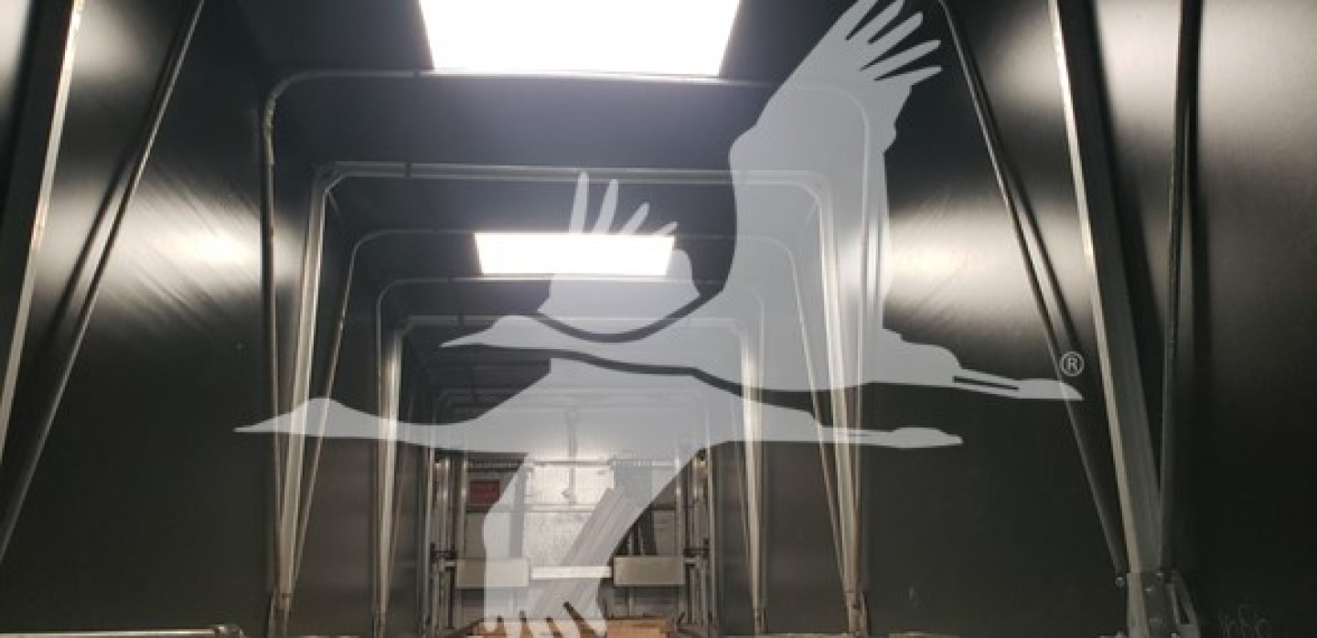 Trailer interior showing steel framework and ventilation opening, reflected branding of a bird logo overlay
