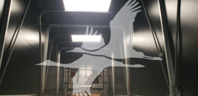 Trailer interior showing steel framework and ventilation opening, reflected branding of a bird logo overlay