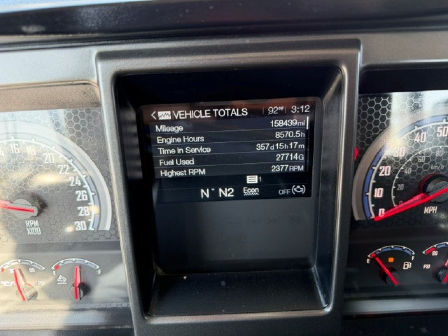 Dashboard display showing vehicle totals: Mileage 158,439 mi, Engine Hours 8,570.5 h, Time In Service 357 days 15 h 17 m, Fuel Used 27,714 gal, Highest RPM 2377, N N 2 gear indicator.