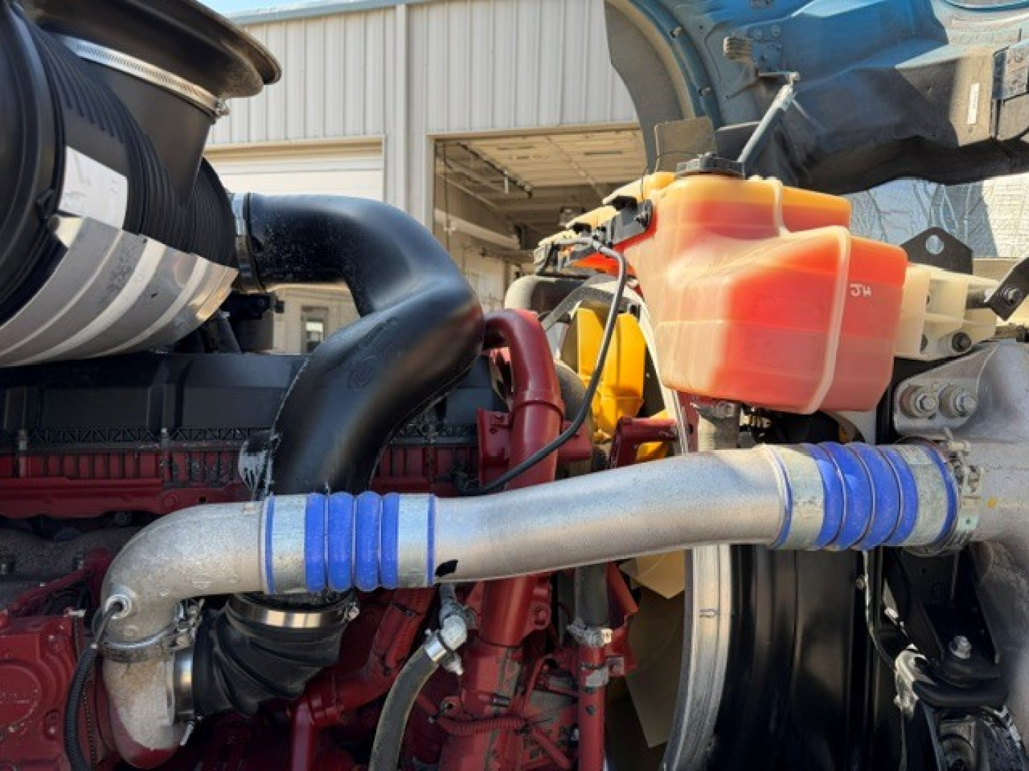 Mack GR64B engine bay showing large intake piping with blue silicone couplers and orange coolant reservoir.