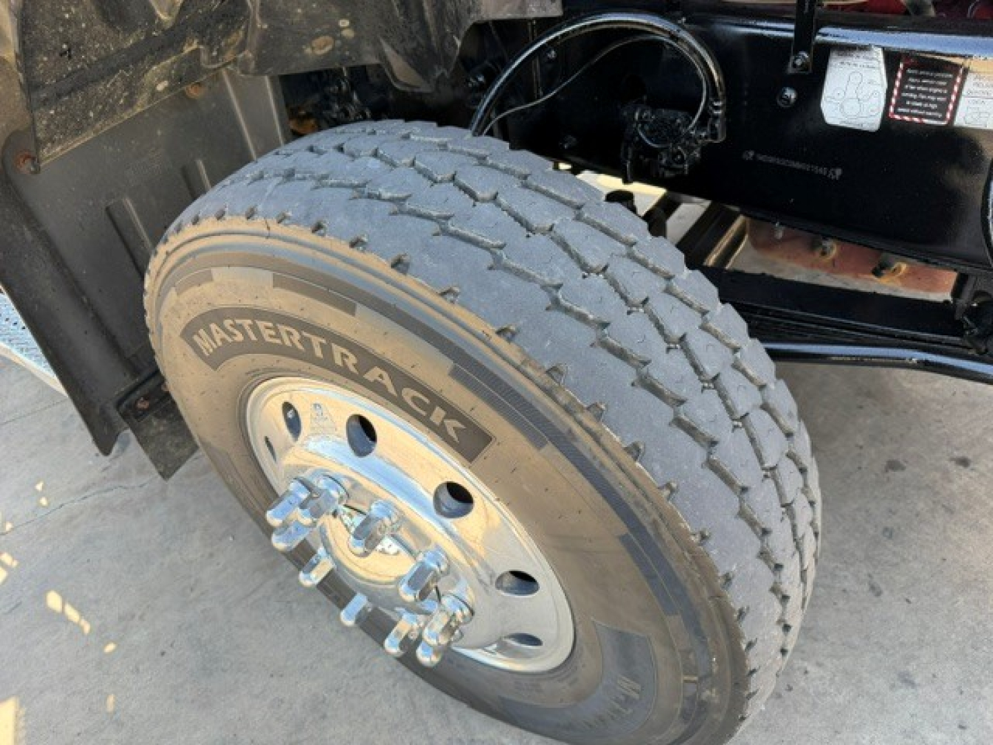 Mack GR64B wheel showing MasterTracK tire and dual front axle components; truck frame and underbody visible in background.