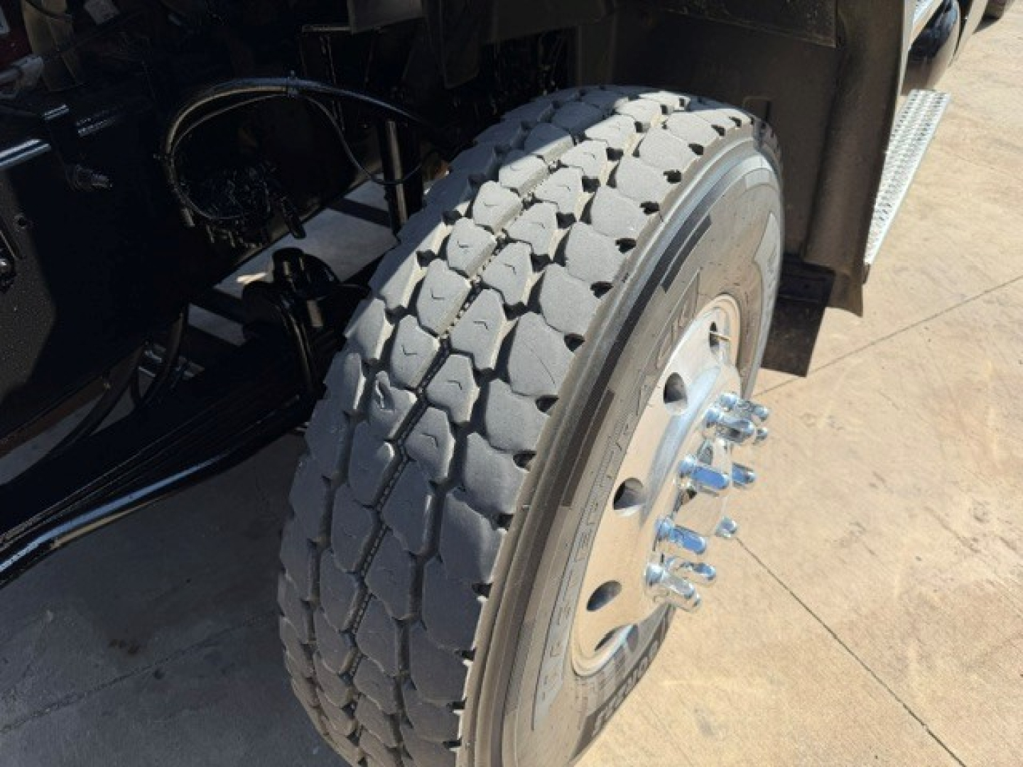 Truck wheel showing large heavy-duty tire and dual axle hub with lug nuts and wheel studs, under a Mack GR64B chassis.