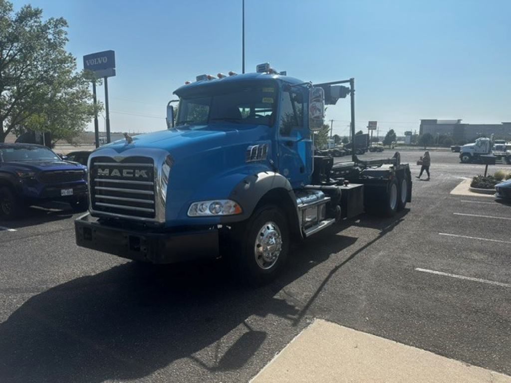 Mack GR64B truck cab and chassis in blue, front grille with MACK letters, wheel tires visible, roadside lot background.