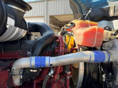 Mack GR64B engine bay showing large intake piping with blue silicone couplers and orange coolant reservoir.