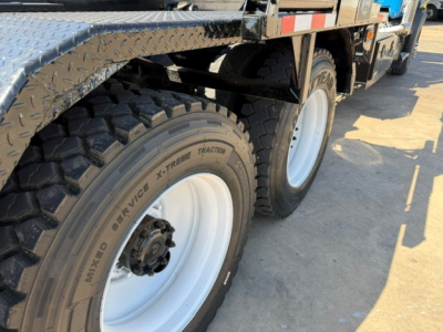 Mack GR64B roll-off truck showing dual rear tires and heavy-duty chassis with diamond plate step and tire tread text visible.