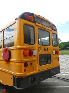 School bus rear view with yellow body, black bumper, red and white taillights, number 344, guard/mounts, and rear window; chain-link fence in background.