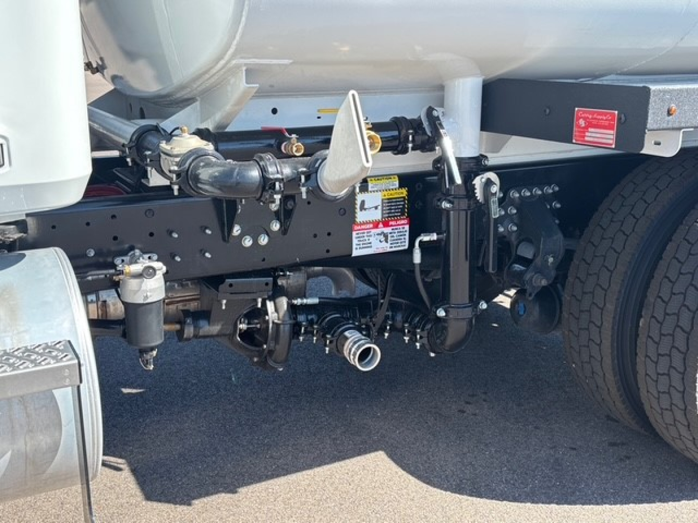 Mack MD7 truck chassis showing suspension, linkage, and fuel tank area with warning labels and connectors visible.
