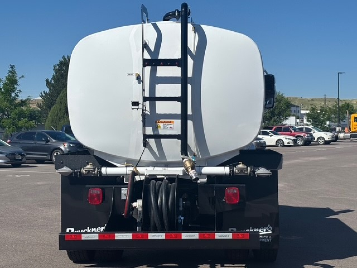 Tank truck rear showing white cylindrical tank, ladder, hose reel, and Mack MD7 tank connection fittings.