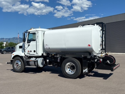 Tank truck chassis showing Mack MD7 cab and cylindrical white tank with rear piping and dual rear wheels.
