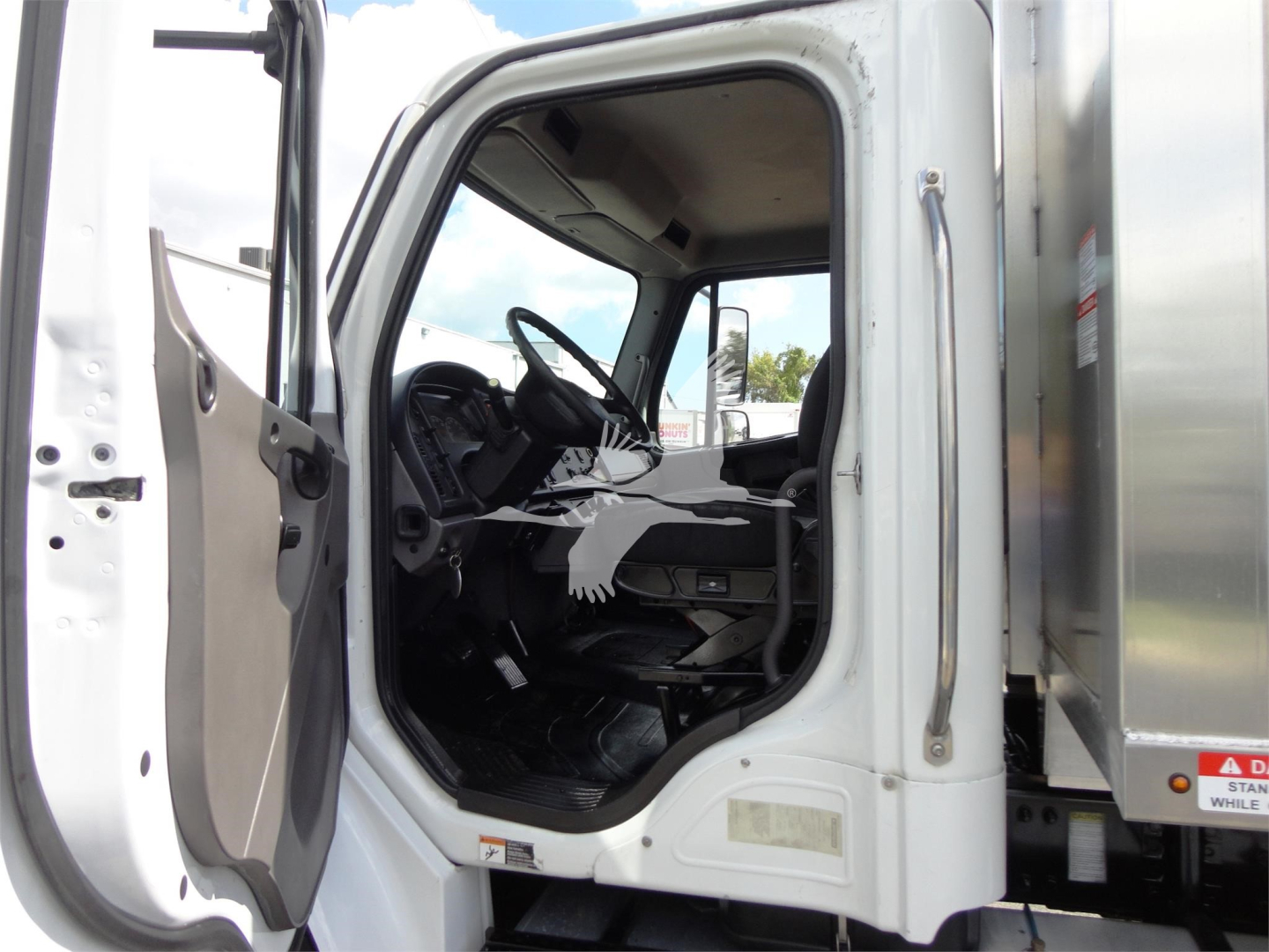 Cab interior of a 2014 Freightliner M2 106 truck showing steering wheel, dashboard, and entry door open.