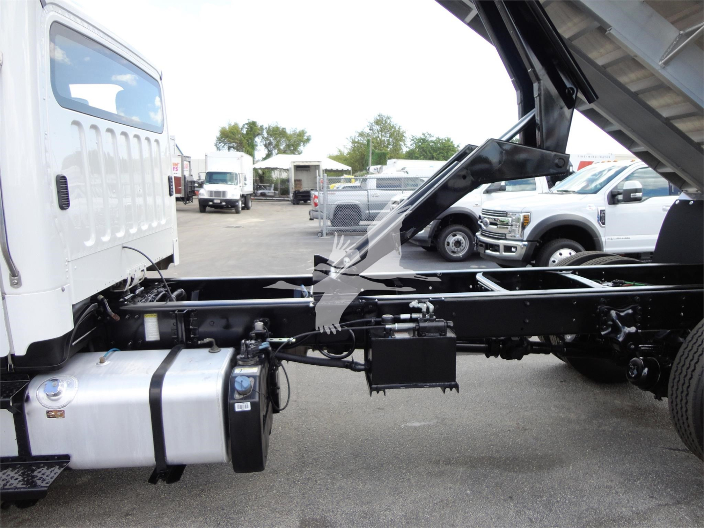 Truck chassis side view of a Freightliner M2 106 with cab tilted for maintenance; visible fuel tank, frame rails, and hydraulic components.