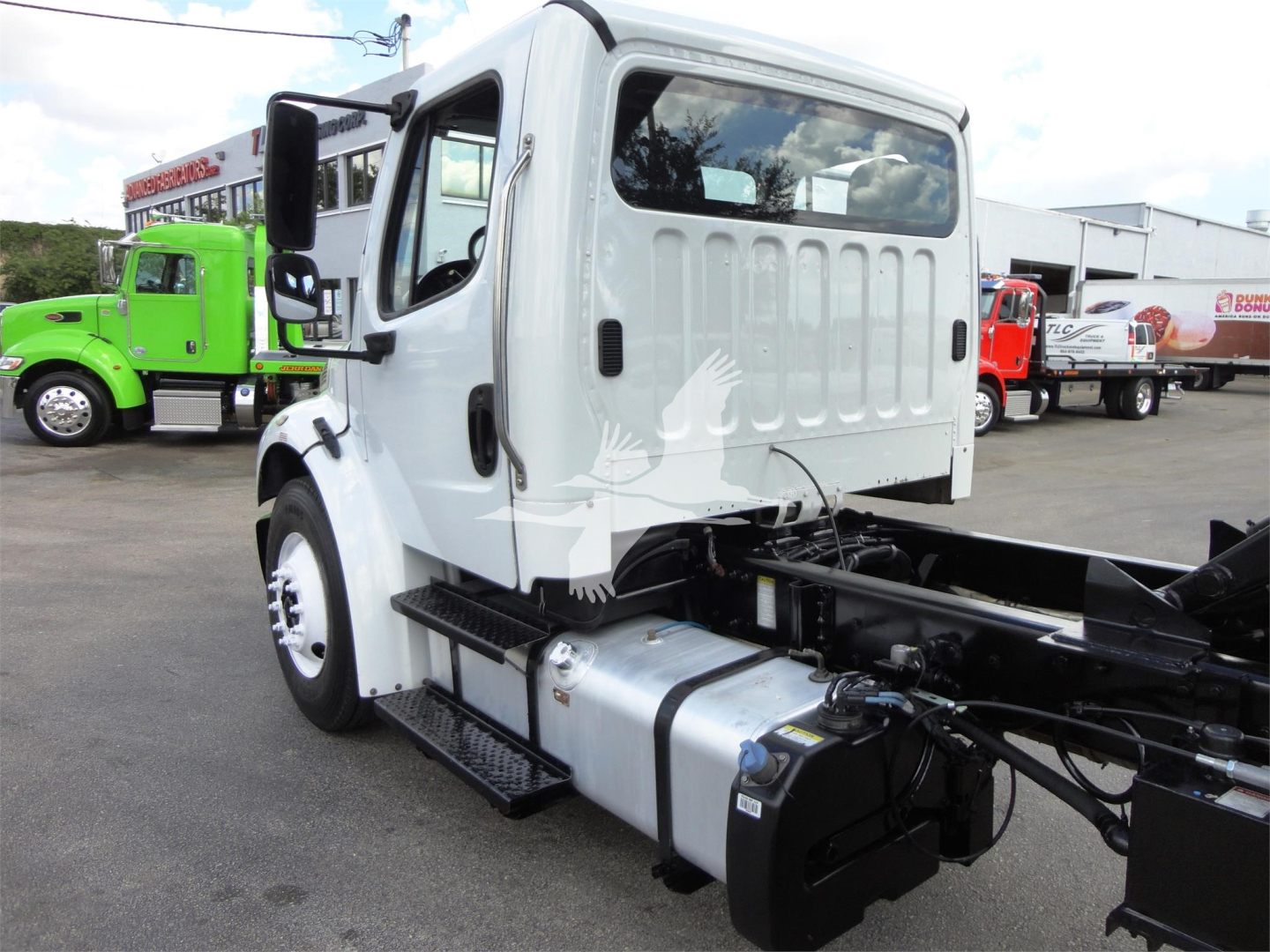 Cab of a white Freightliner M2 106 chassis showing fuel tank and engine bay area with exposed frame and side steps.