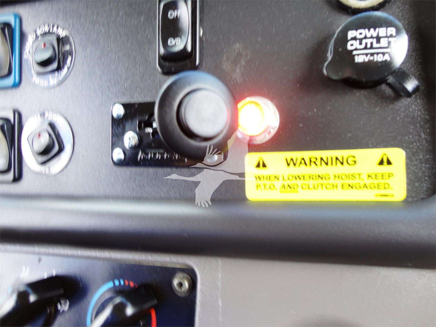 Cab controls and warning label inside a Freightliner M2 106 dashboard area showing ignition switch, power outlet, warning sticker, and control knobs.