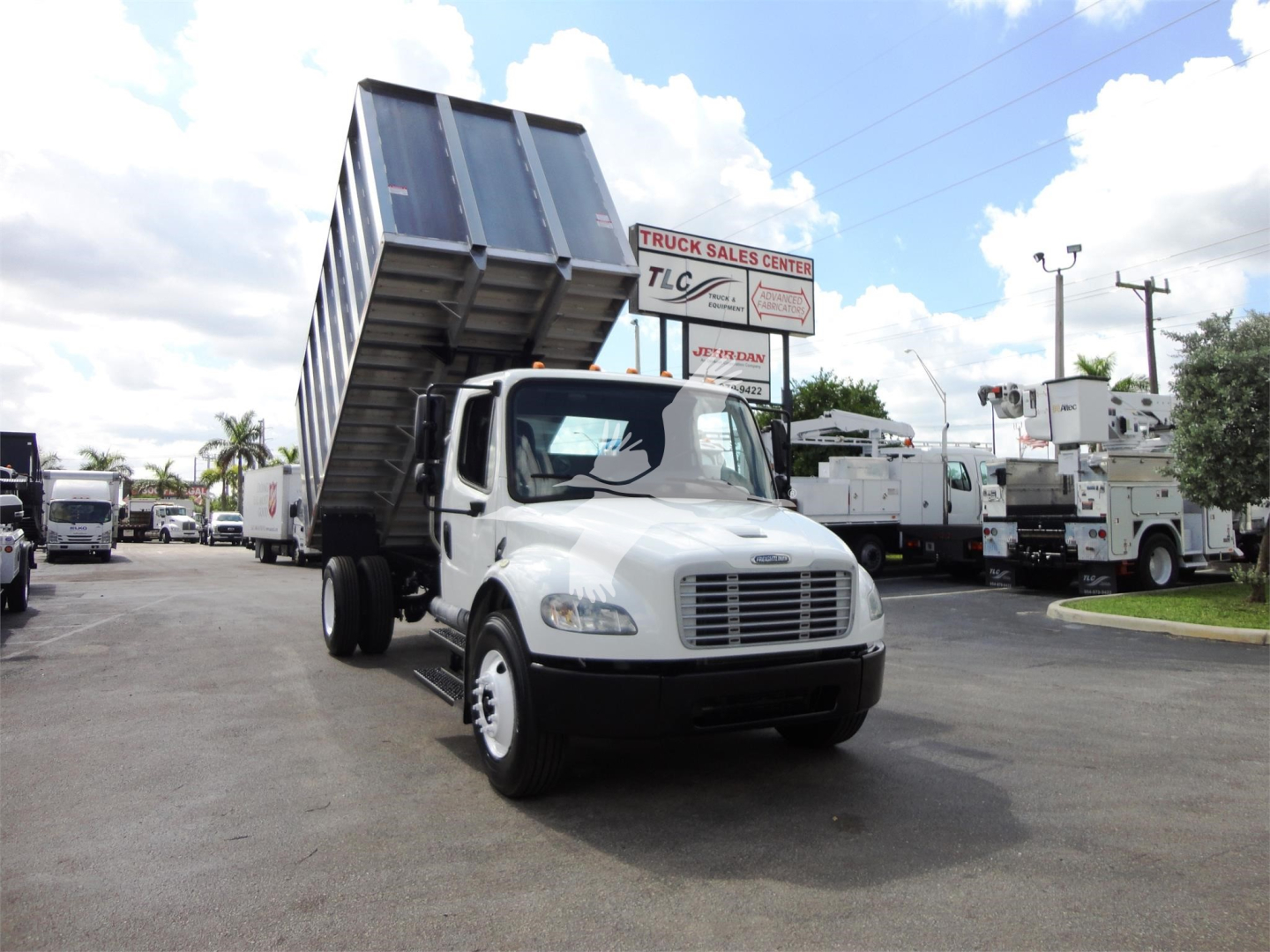 Truck with raised tipping bed in a dealership lot showing Freightliner M2 106 cab and dump bed raised