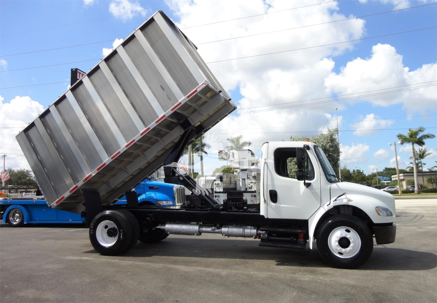 Truck chassis with a raised dump bed on a white Freightliner M2 106 dump truck, side view showing cab, hydraulic system, and dumping bed.
