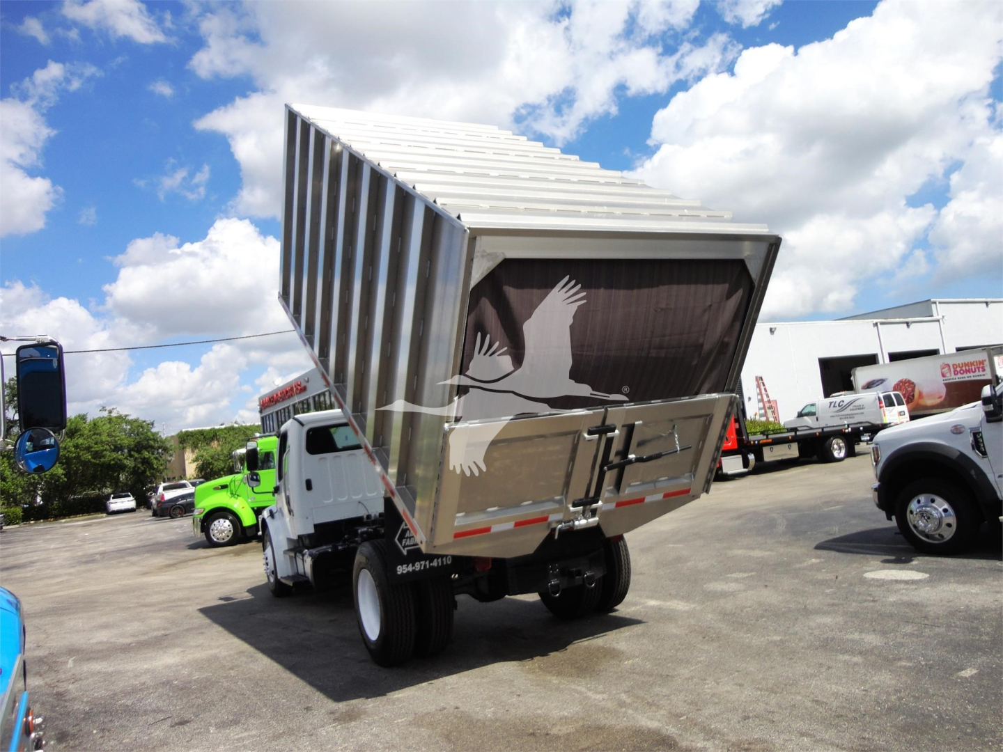 Freightliner M2-106 dump truck bed raised in yard with other trucks nearby