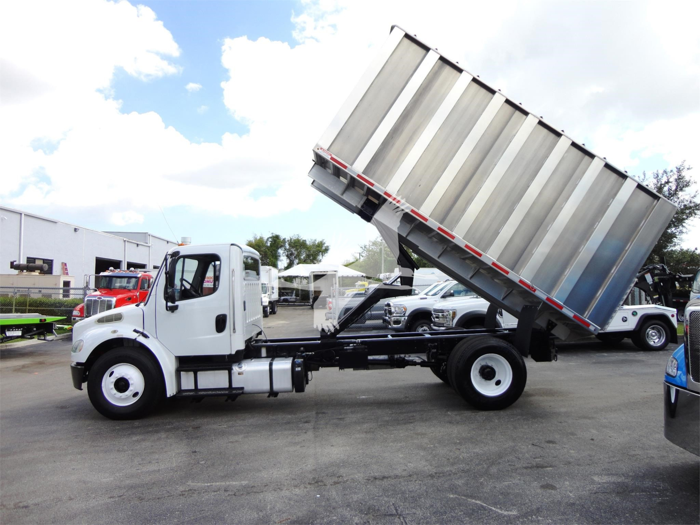 Freightliner M2 106 dump truck chassis with raised dump bed in a dealership lot.