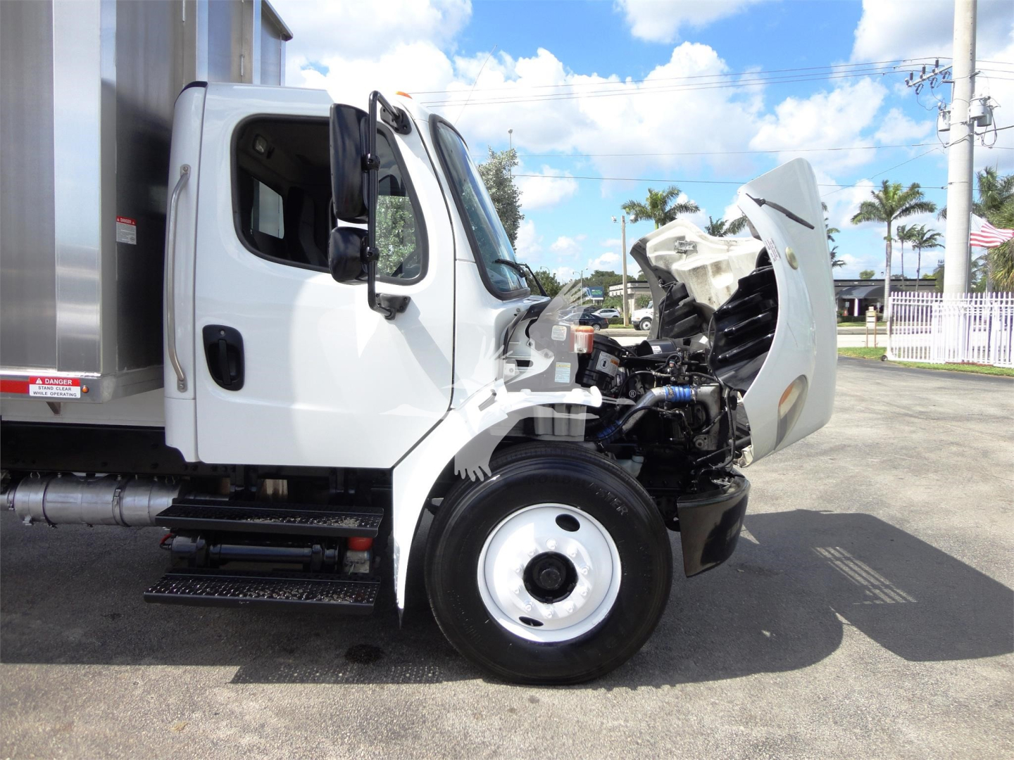 Side view of a 2014 Freightliner M2 106 truck with the hood open, showing engine compartment and front wheel.