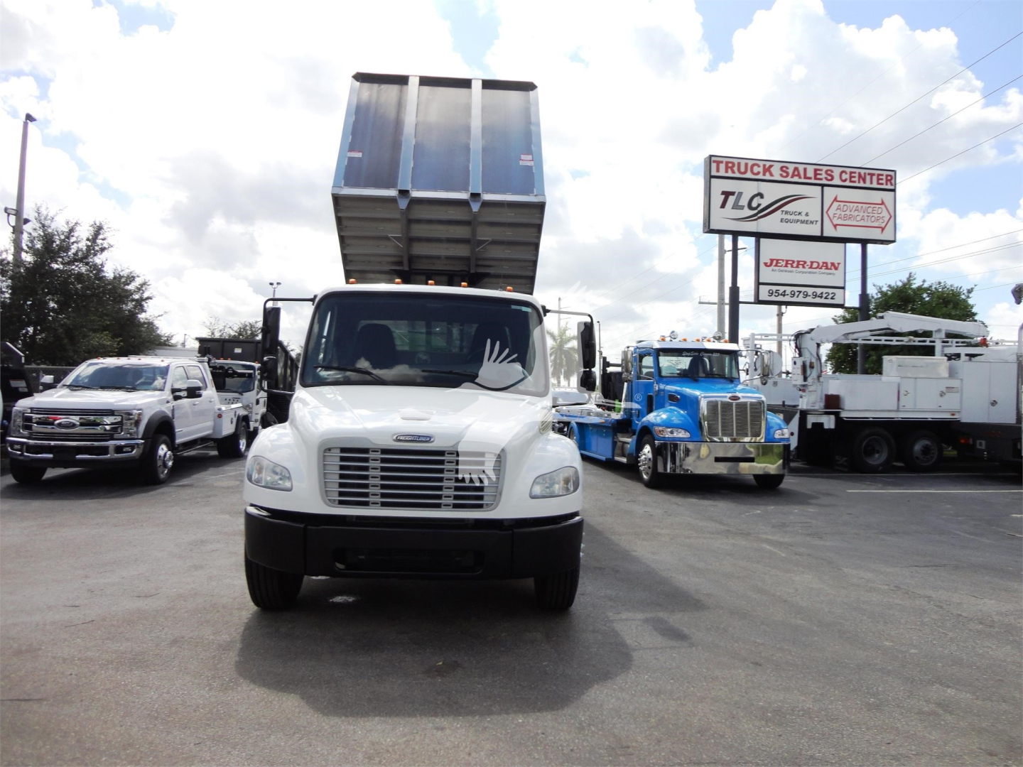 Front view of a 2014 Freightliner M2 106 dump truck with raised bed in a dealership lot, other trucks visible in background.