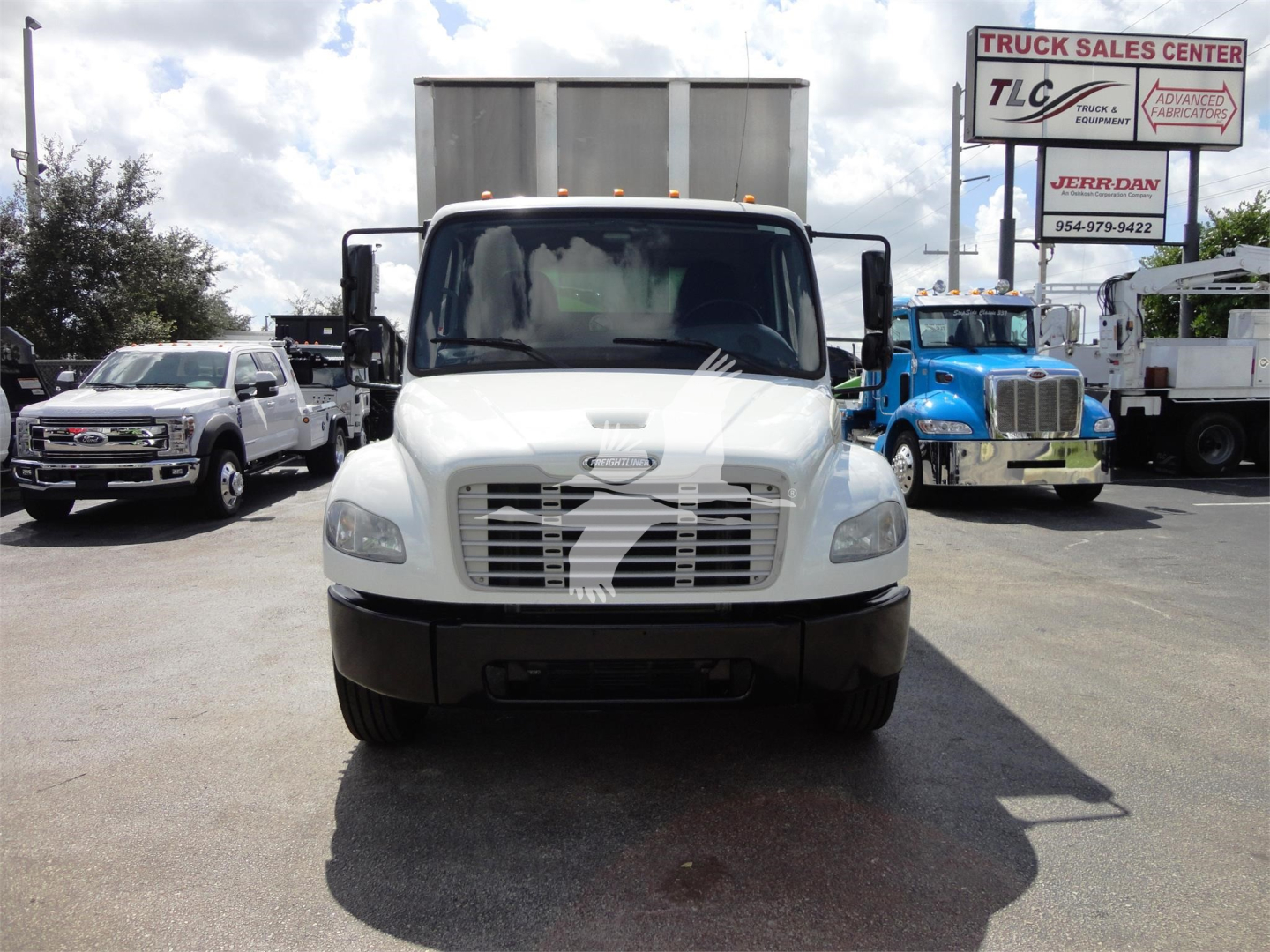 Truck front view of a white Freightliner M2 106 in a dealership lot with other trucks in background.