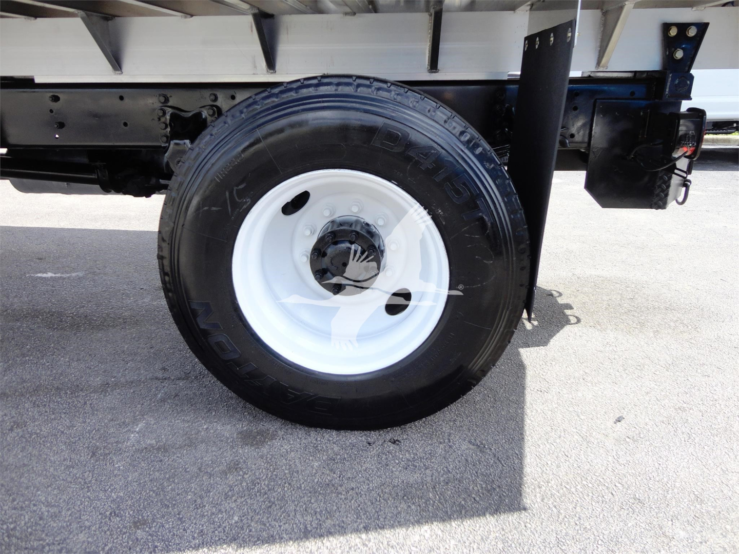 Wheel and chassis section of a Freightliner M2 106 truck showing front wheel with white rim and tire, undercarriage and chassis components.