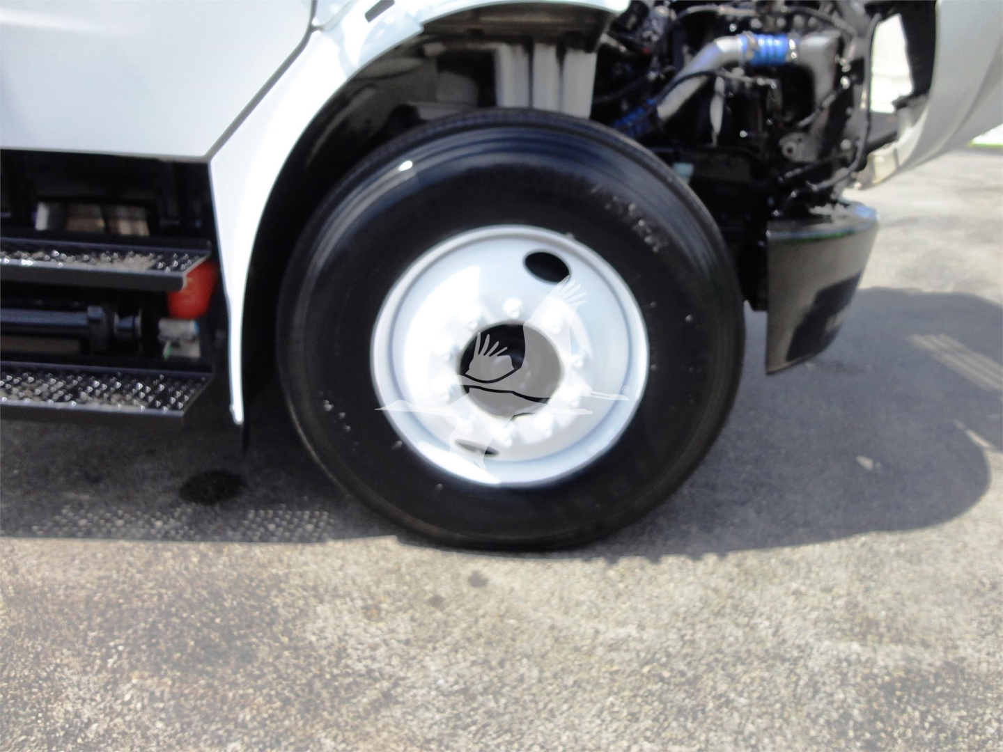 Fleet truck front wheel and cab area showing wheel hub and tire with engine bay visible.
